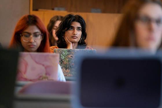 Photo of a female Chatham University student standing in front of her presentation, as two professors offer thoughts.